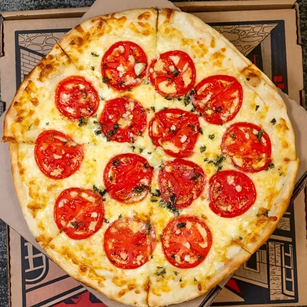 Massimo's Beachside Pizza's Margherita pizza, topped with fresh tomatoes, mozzarella, and basil, in a box.