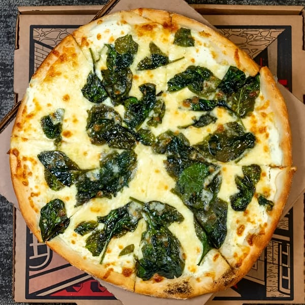 Massimo's Beachside Pizza's white pizza with spinach, cut into slices, in a pizza box.