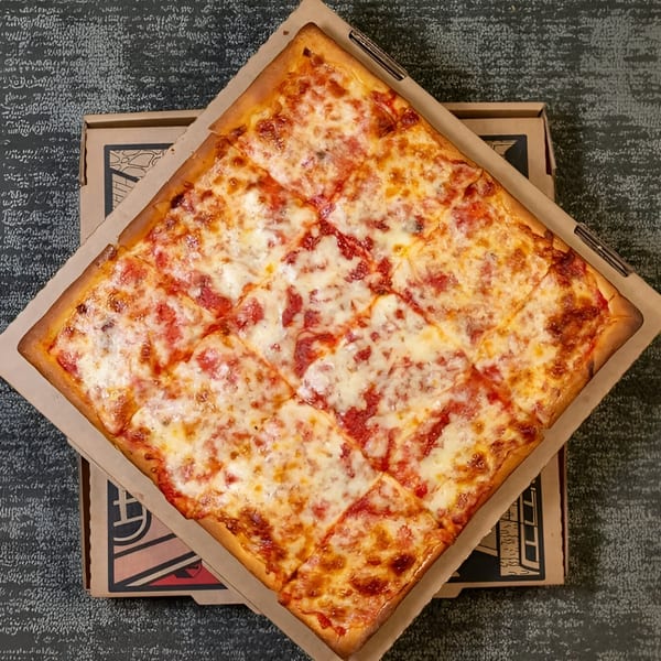A square Massimo's Beachside Pizza, cut into squares, sits in a cardboard box.