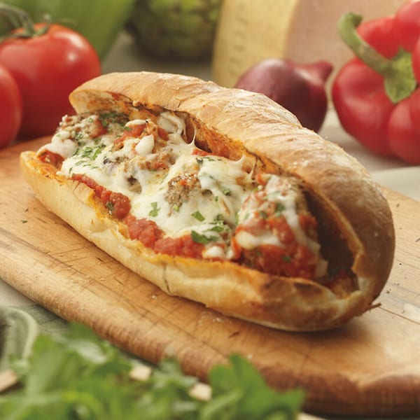 Massimo's Beachside Pizza's meatball sub, with melted cheese and tomato sauce, on a wooden board.